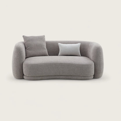 Divano dal design moderno e elegante in tessuto tortora con forma curva e asimmetrica, divano imbottito, braccioli avvolgente e confortevoli con angoli arrotondati e schienale pulito con cuciture curate.