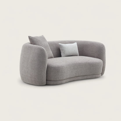 Divano dal design moderno e elegante in tessuto tortora con forma curva e asimmetrica, divano imbottito, braccioli avvolgente e confortevoli con angoli arrotondati e schienale pulito con cuciture curate.